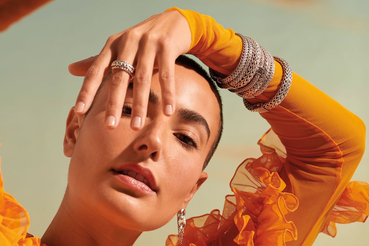 A woman wearing multiple John Hardy bracelets, an earring, and ring.