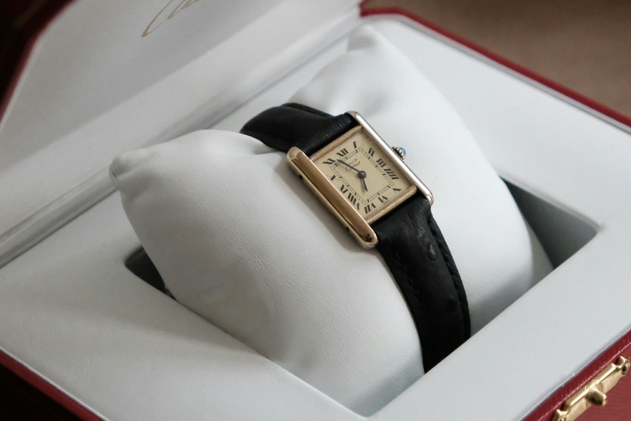 a yellow gold Cartier Tank watch with a black strap on a white pillow in a box