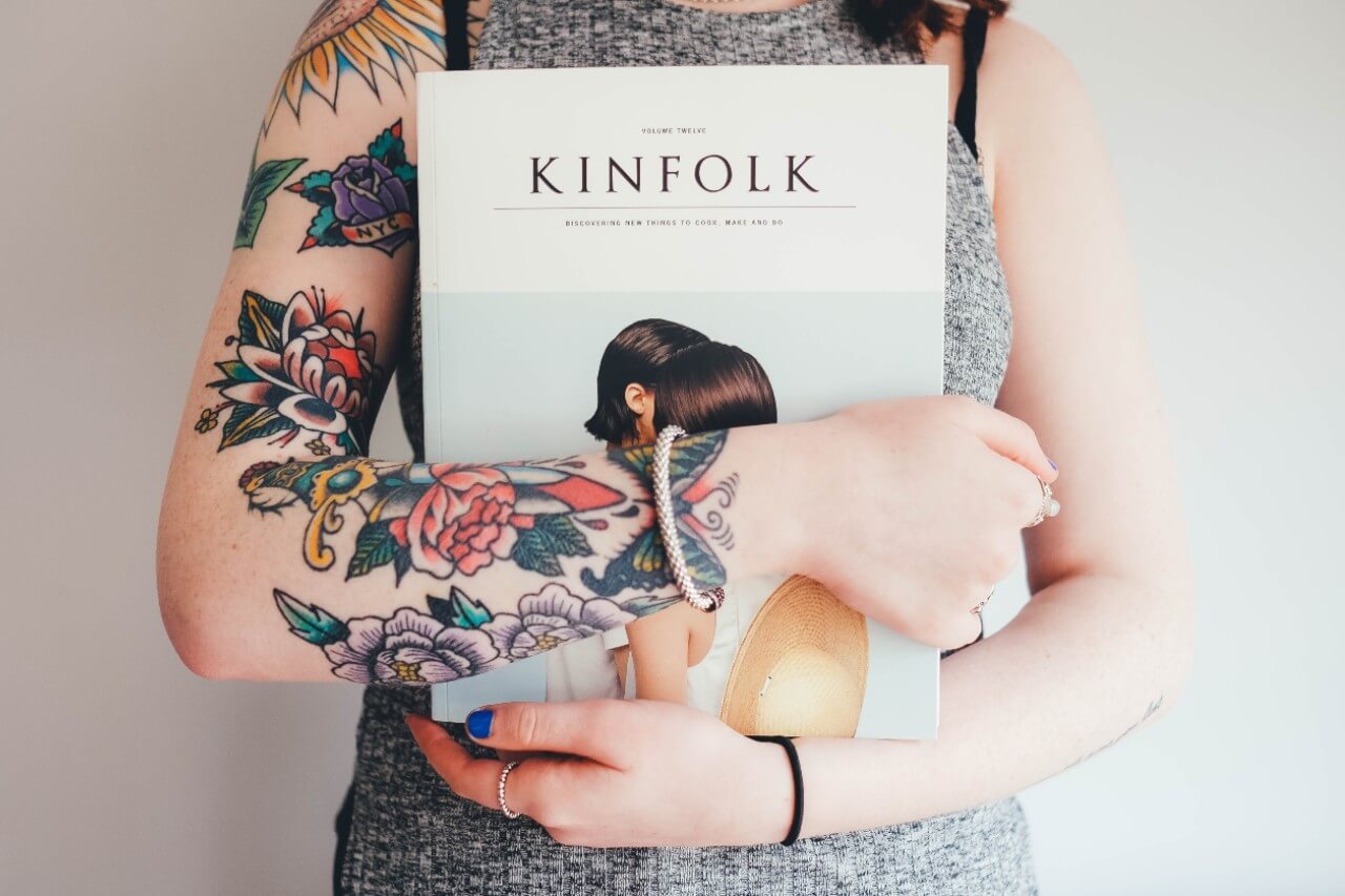 A tattooed woman wearing a bangle holding a photography magazine.