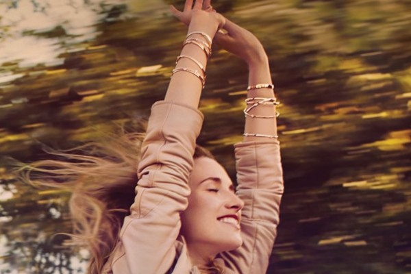 Woman wearing multiple Hearts On Fire bracelets with her arms raised in the air and eyes closed as she’s driving down the road and she’s through the sunroof.